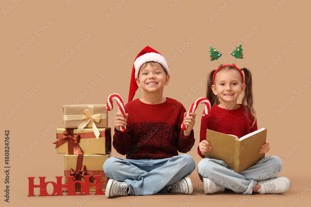 Naklejka premium Cute little children with book and Christmas gifts sitting on beige background