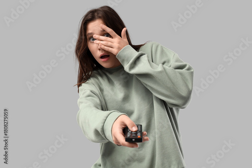 Scared young woman watching TV on light background