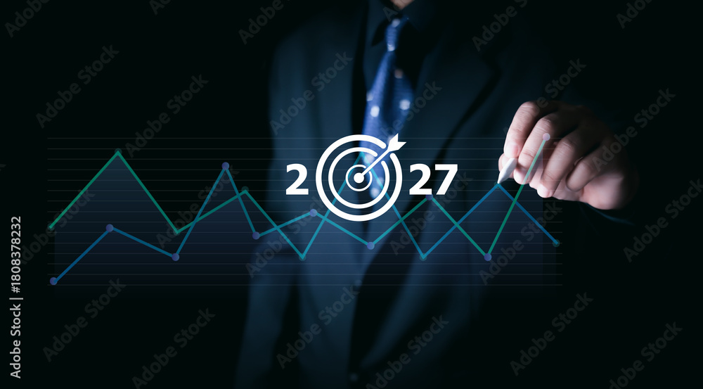 Fototapeta premium Businessman pointing at digital target icon with 2027 and rising line graph, symbolizing future strategy, financial growth, data analytics, corporate planning, and market performance trends.