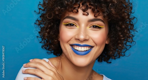 Young Woman with Bright Blue Lipstick and Yellow Eyeliner Smiling Happily Against a Blue Background