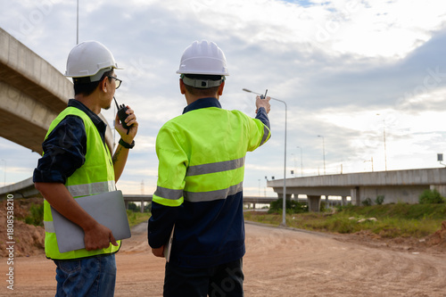 Fotografi Construction engineers supervising road construction work, coordinating with walkie talkies and inspecting elevated highway infrastructure during field operation
