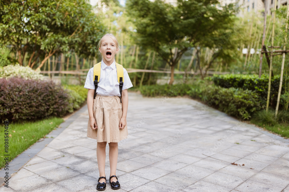 Naklejka premium Schoolgirl back to school after summer vacations. Pupil in uniform smiling early morning outdoor.