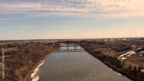 Wallpaper Mural North Saskatchewan River flows toward Edmonton as early sunrise light casts warm tones across calm water and distant bridges creating peaceful prairie edge scene captured from steady drone view. Torontodigital.ca