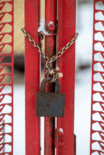 Old rusty padlock hanging on a bright red metal gate with a chain in winter