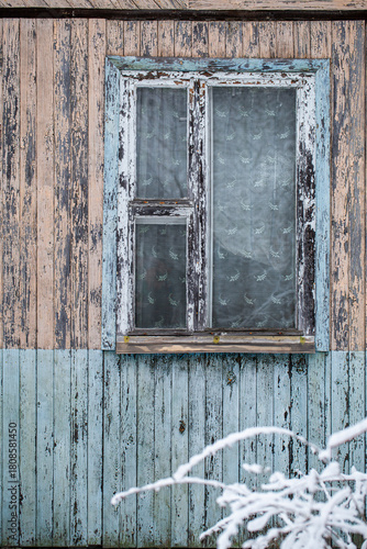 Old rustic window with peeling blue paint on a weathered wooden wall in winter