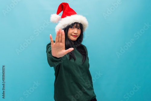 Asian woman in Santa hat raises her hand signaling stop playfully Ideal for Christmas safety tips and fun festive visuals