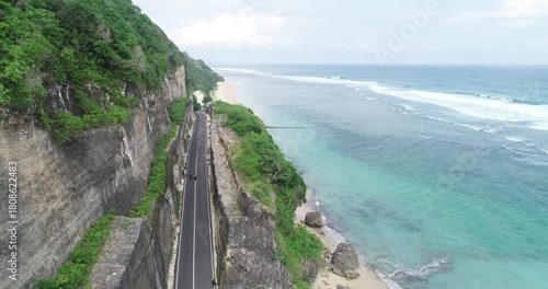 Aerial view of the blue sea, green trees, and coastal road.
