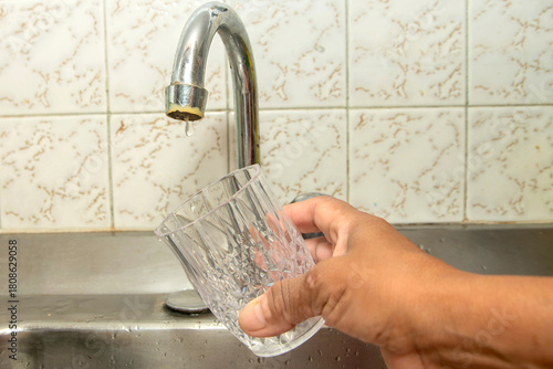 Obraz na płótnie Close-up of a hand holding a glass under a dry kitchen tap
