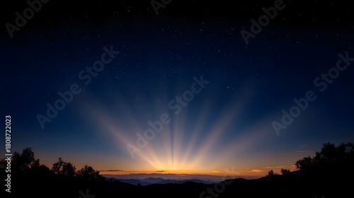 Vibrant sunrise with crepuscular rays bursting over silhouetted mountains and trees against a starry twilight sky