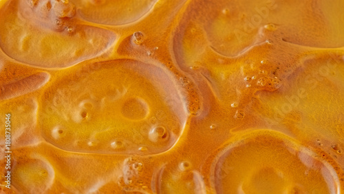 Bubbling golden syrup fills a pot, creating an inviting scene of rich textures and deep colors. The heat transforms the ingredients, highlighting their warmth and sweetness