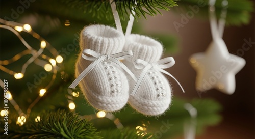 Small white knitted baby booties hanging on a green christmas tree branch with lights