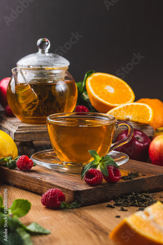 Tea in a glass mug on the table next to mint, raspberries and fruits