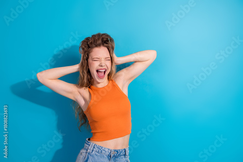 Quadro su tela Young woman in orange crop top poses joyfully against blue background for lifest