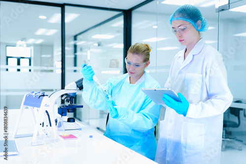 scientists collaborate on assay development, with one performing a critical pipetting step while the other documents the procedure on a tablet for protocol validation under GxP guidelines.