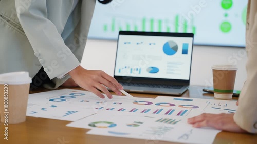 Business team collaborating on financial data and analytics in a modern office. Two colleagues are reviewing charts and graphs while discussing results with a laptop data visuals in the background