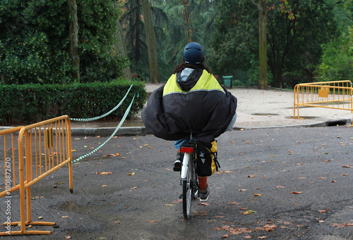 Bild auf Leinwand Montando en bicicleta con abrigo poncho, capucha y chubasquero impermeable bajo