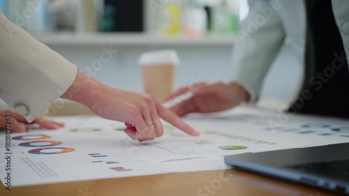 Close-up of two business women analyzing financial data on charts and laptop screen during a team meeting