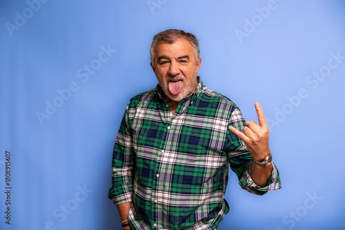 Senior man showing rock and roll gesture sticking out tongue