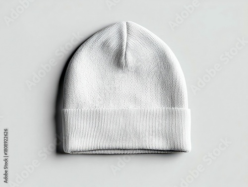 A close-up, overhead shot of a plain white knit beanie hat, folded at the brim, resting on a smooth, light gray surface.