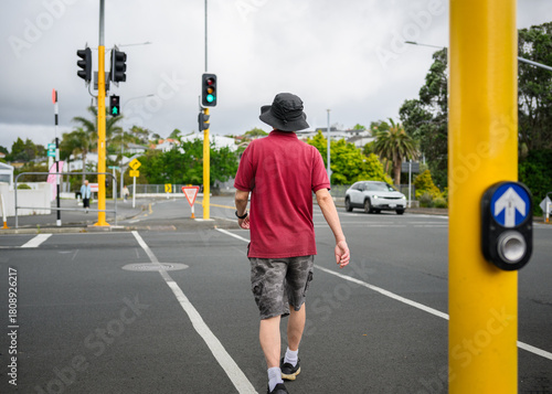 Man walking across the street with green pedestrian crossing light on. Auckland.