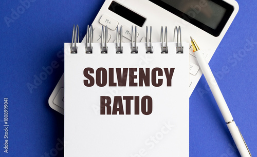 Notepad with text solvency ratio placed on top of calculator and pen on blue background