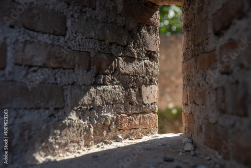 Close-up low-angle view through a narrow opening in a weathered brick wall, revealing a historic ruin or abandoned structure. Texture, decay, and architectural detail