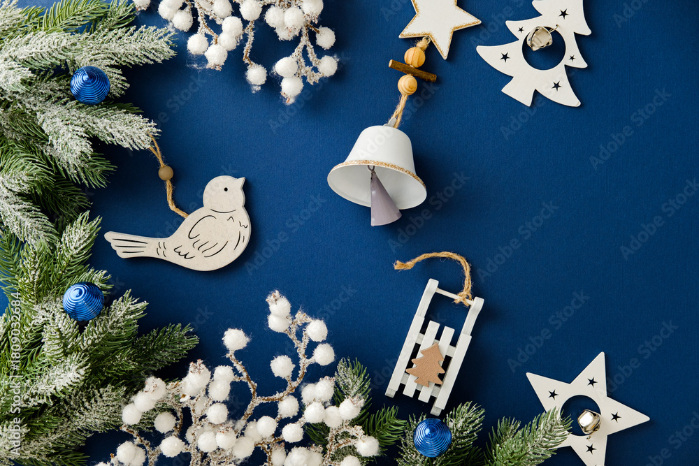 Obraz premium Christmas flat lay with wooden toys, bell, and frosted fir on blue background