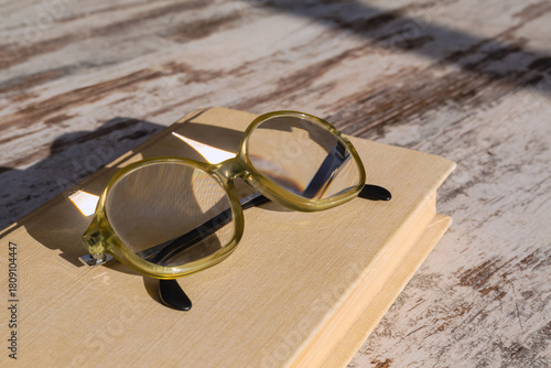 Old-fashioned reading glasses with high optical power lenses for nearsightedness lying on a book in bright sunlight, close-up.