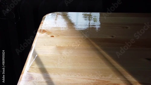 Applying glossy varnish to wooden surface with brush in sunlit room
