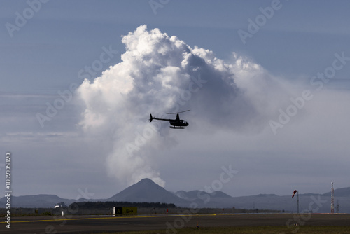 View of a helicopter soaring against a backdrop of billowing white clouds and distant mountains, a dance of machinery and nature's grandeur, Reykjavík, Reykjavíkurborg, Iceland.