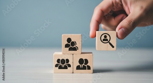 Hand placing a wooden block with a magnifying glass icon on top of other blocks with people icons.