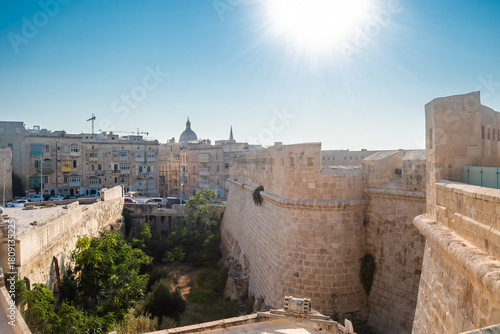 Sturdy ramparts of Fort St. Elmo and moat, with traditional architecture in the background and shinning sun, Valletta MALTA