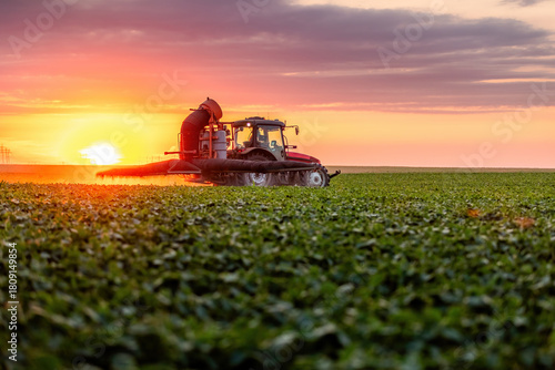 Tractor spraying pesticide in agriculture field at sunset