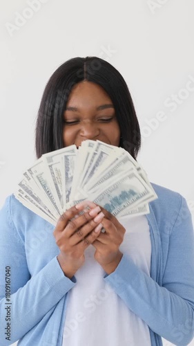 Portrait of an excited young African American woman holding a fan of hundred dollar bills. She is smiling and showing off cash isolated on white background.