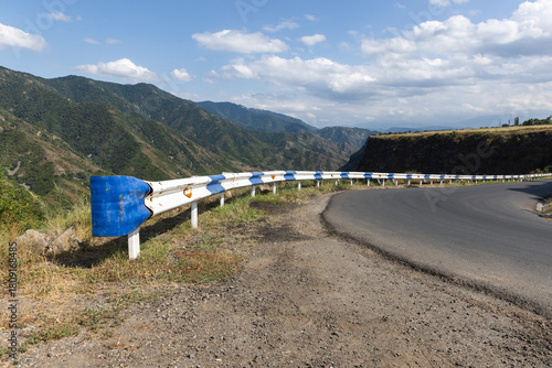 Foto Winding mountain road hugs a cliff, protected by blue and white guardrails