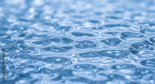 Close-up of rippling water surface, creating a textured pattern with light reflections and subtle blue hues.
