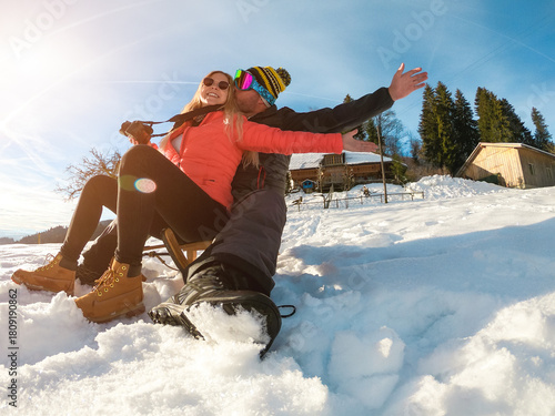 Happy influencer couple having fun with wood vintage sledding on snow high mountains - Young people enjoy winter vacation - Travel, love and holiday concept - Soft focus on faces