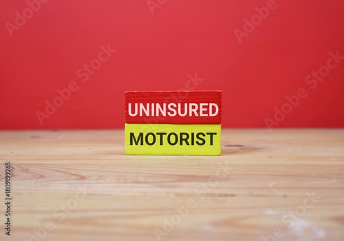 Slika na platnu two wooden blocks labeled Uninsured and Motorist, stacked on a wooden table against an red background