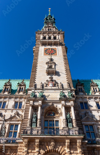 The impressive clock tower and main entrance of Hamburg City Hall in Germany, captured on a clear, sunny day against a bright blue sky