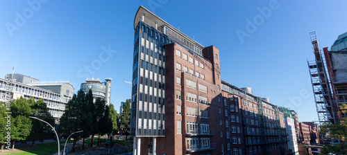 A modern office building with a curved glass and brick facade, contrasting with surrounding contemporary architecture in the urban area of Hamburg, Germany