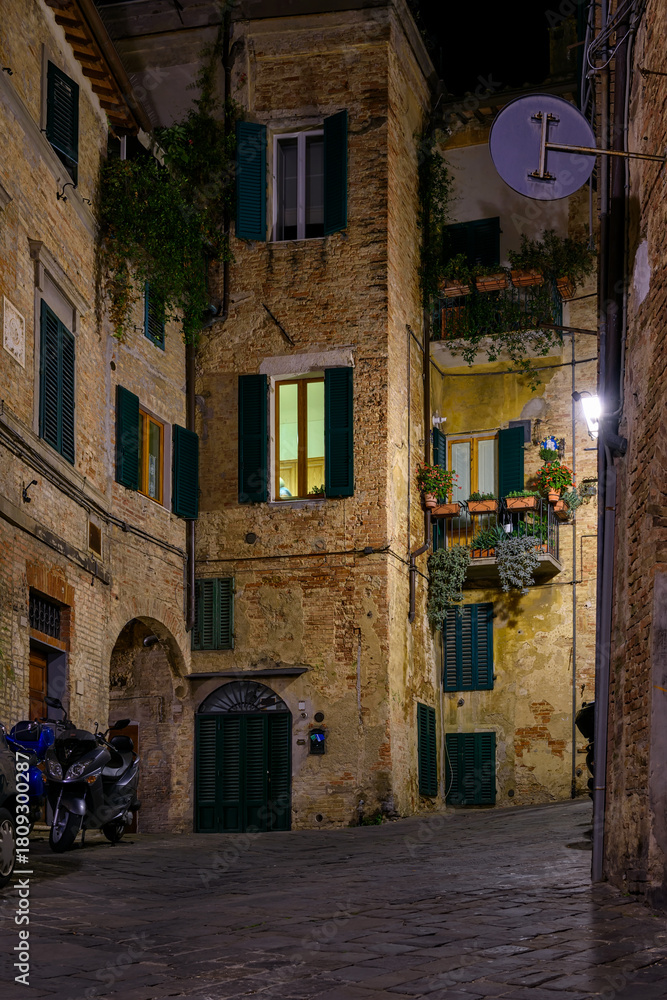 Fototapeta premium Medieval narrow street in Siena at night, Tuscany, Italy. Architecture and landmark of Siena. Cozy cityscape of Siena