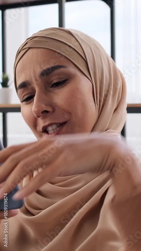 Close-up portrait of happy young Muslim woman in hijab using smartphone. Cheerful female looking at phone screen, reading good news or watching funny video.