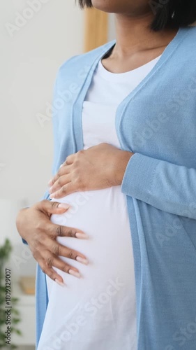 Portrait of a happy pregnant young African American woman gently caressing her baby bump. She is smiling and dreaming about her baby isolated on home background.