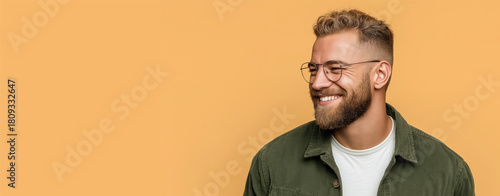 Curly haired man smiles by yellow wall. copy space