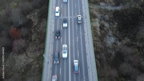 Aerial view of cars traveling on a highway at evening, showcasing dynamic movement. Autos riding at road surrounding landscape and country structure. Automobiles drive at route during journey