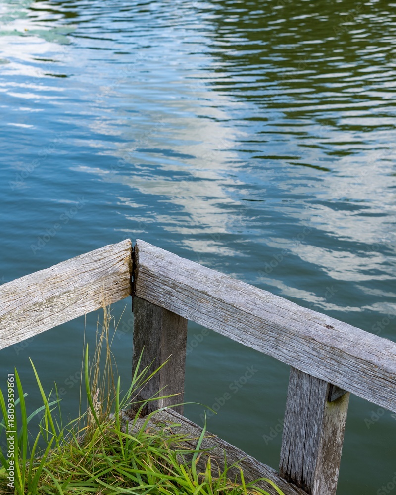 Fototapeta premium Wooden pier corner overlooking calm lake with water lilies and cloud reflections