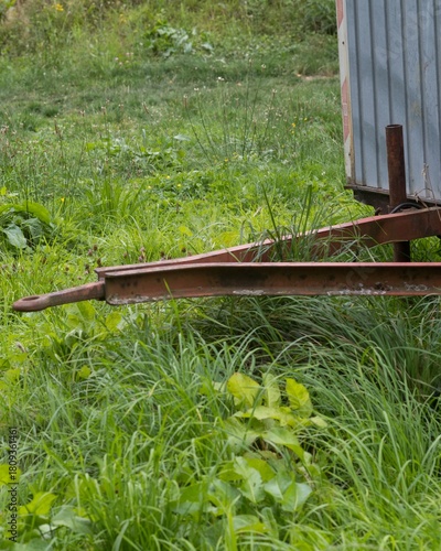 Rusty trailer hitch resting on overgrown grass in backyard