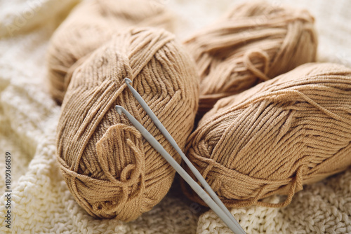 Crochet hooks and balls of beige and brown yarn on white knitted background. Knitting, crocheting supplies.