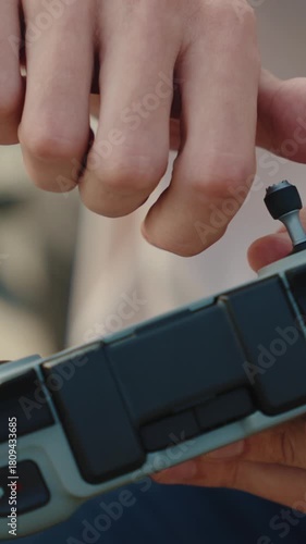A man screws a joystick into a drone controller in a vertical close-up shot on a sunny outdoor day.