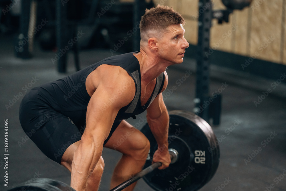 Fototapeta premium Side view. Athletic man performing weightlifting exercises with a barbell in a gym